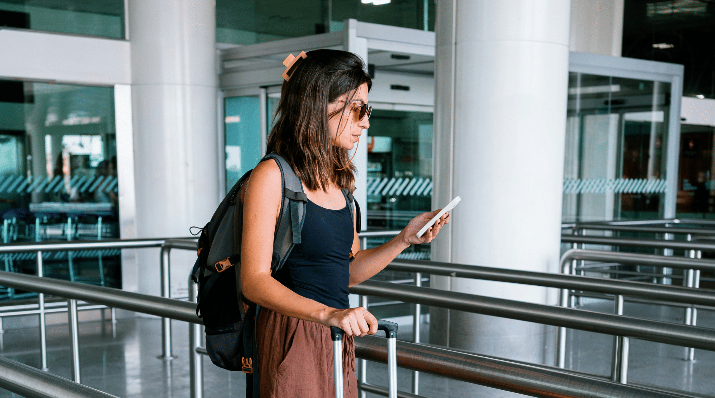 Viajante no aeroporto de Guarulhos usando o celular com chip internacional e carregando mala de bordo.