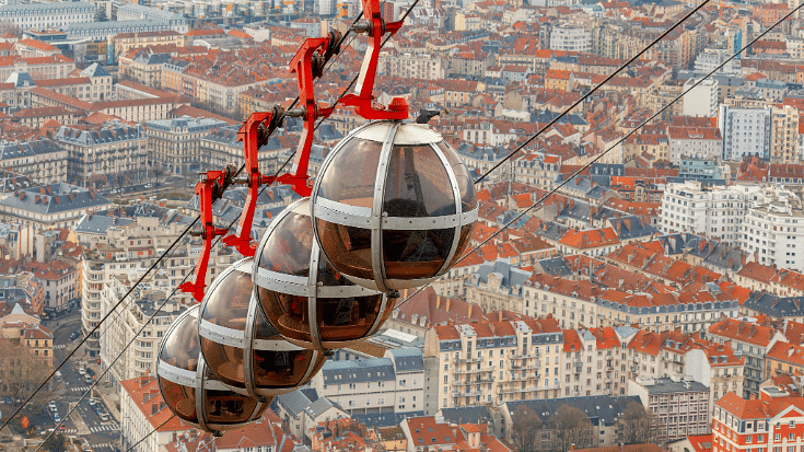 An image of some futuristic looking round cable cars on a row climbing over beautiful buildings above the French alps town of Grenoble to illustrate a blog post entitled The Best Family Winter Holidays From Ireland.