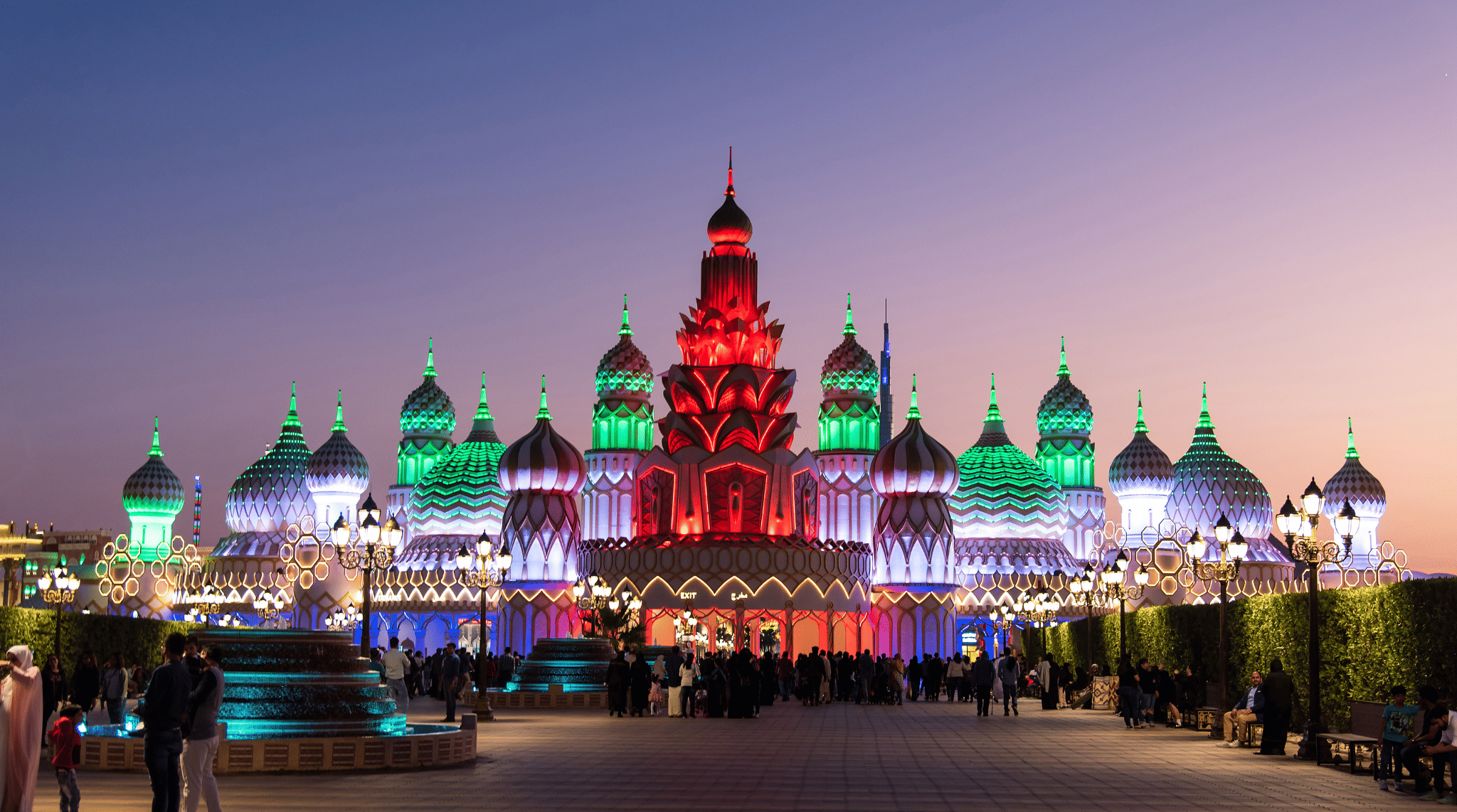 إضاءة مذهلة لبوابة القرية العالمية دبي عند الغروب مع حشود الزوار وألوان مبهرة تعكس أجواء الموسم في 2025