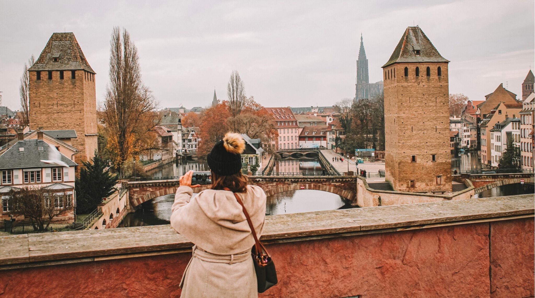 Imagem de uma mulher tirando uma foto das famosas Ponts Couverts em Estrasburgo.