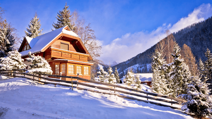 An image of an idyllic snow-covered log cabin on a Swiss mountainside in the deep snow with bright blue skies overhead to illustrate a blog post entitled The Best Family Holidays in Winter from Ireland.