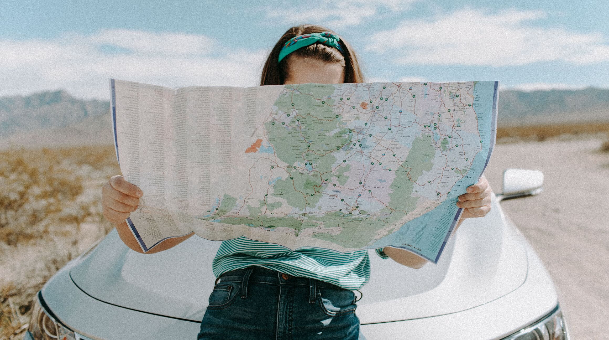 Girl sitting on the hood of a car and looking at a roadmap