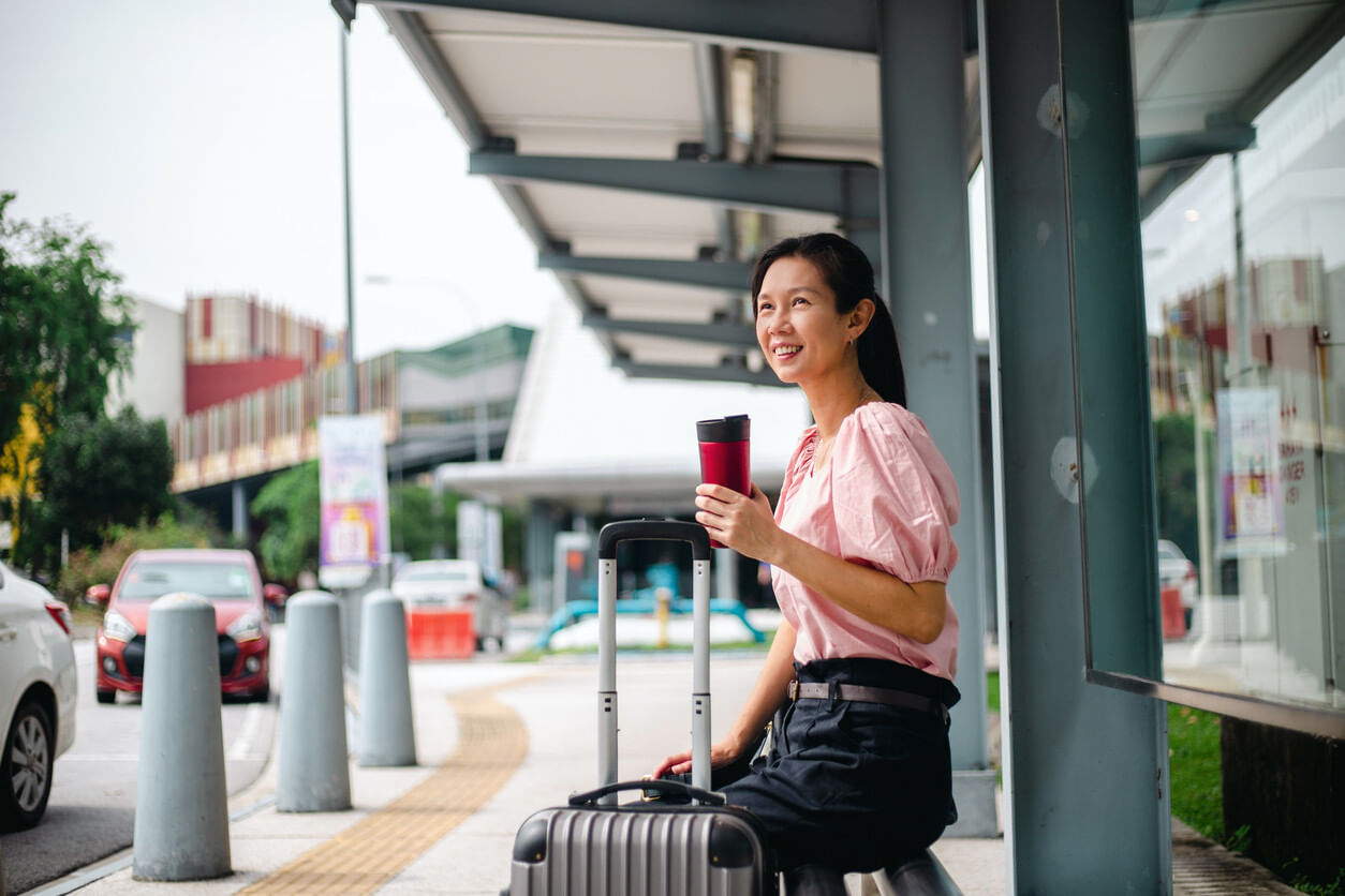 Woman sitting with a suitcase by her side and a tumbler in her hand