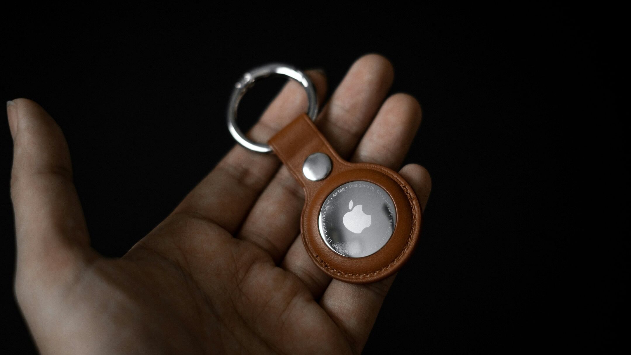 A hand holding a single Apple AirTag against a black background