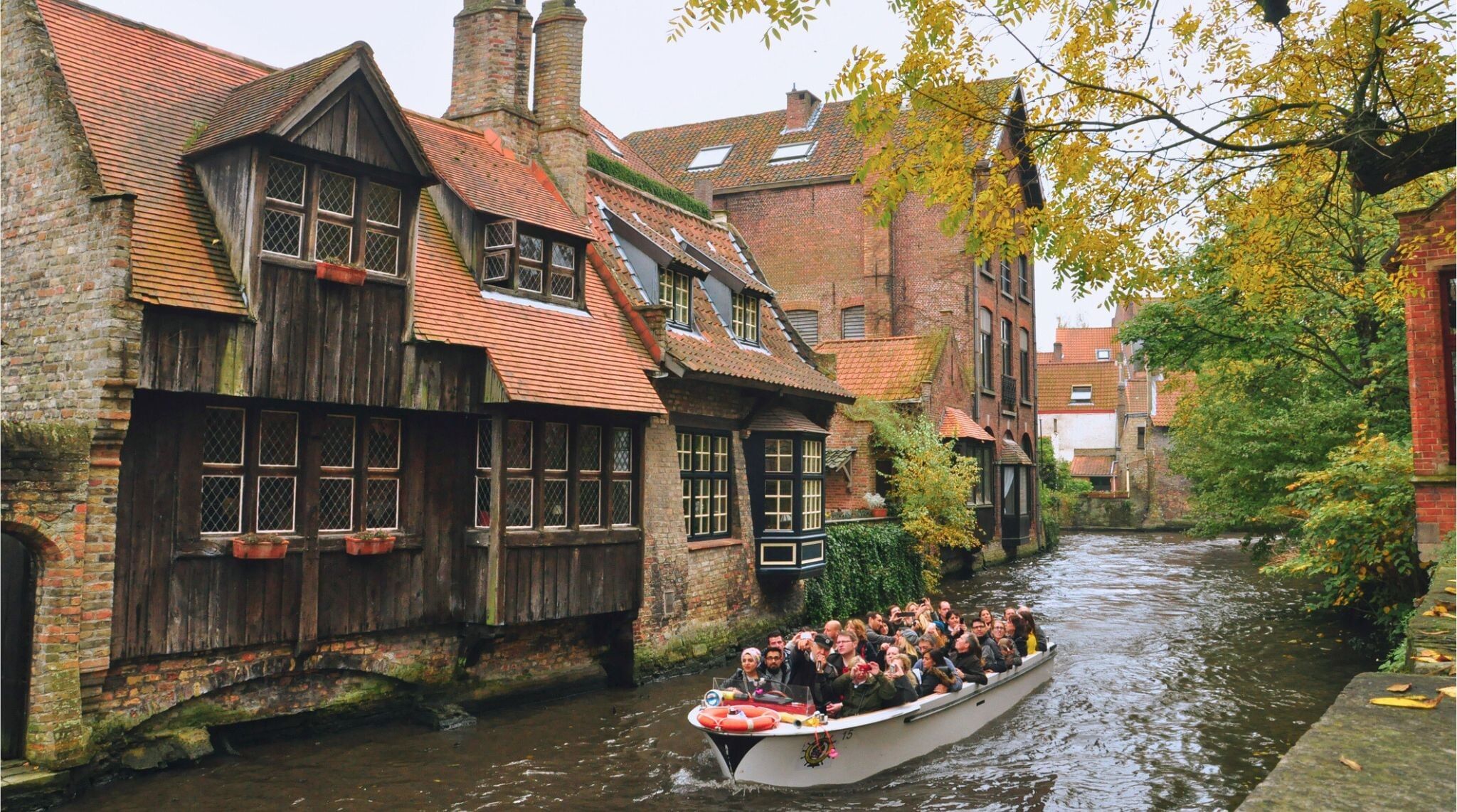 Viajantes em barcas pelos canais de Bruges cercados de prédios de arquitetura medieval.