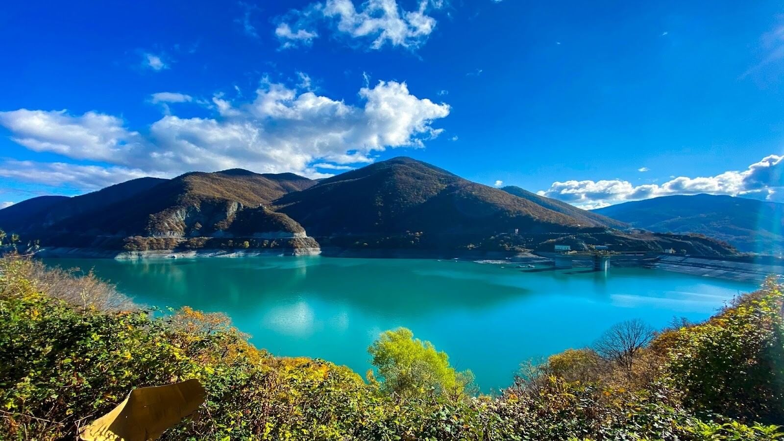 A lake surrounded by mountains and vegetation under a blue sky during daytime