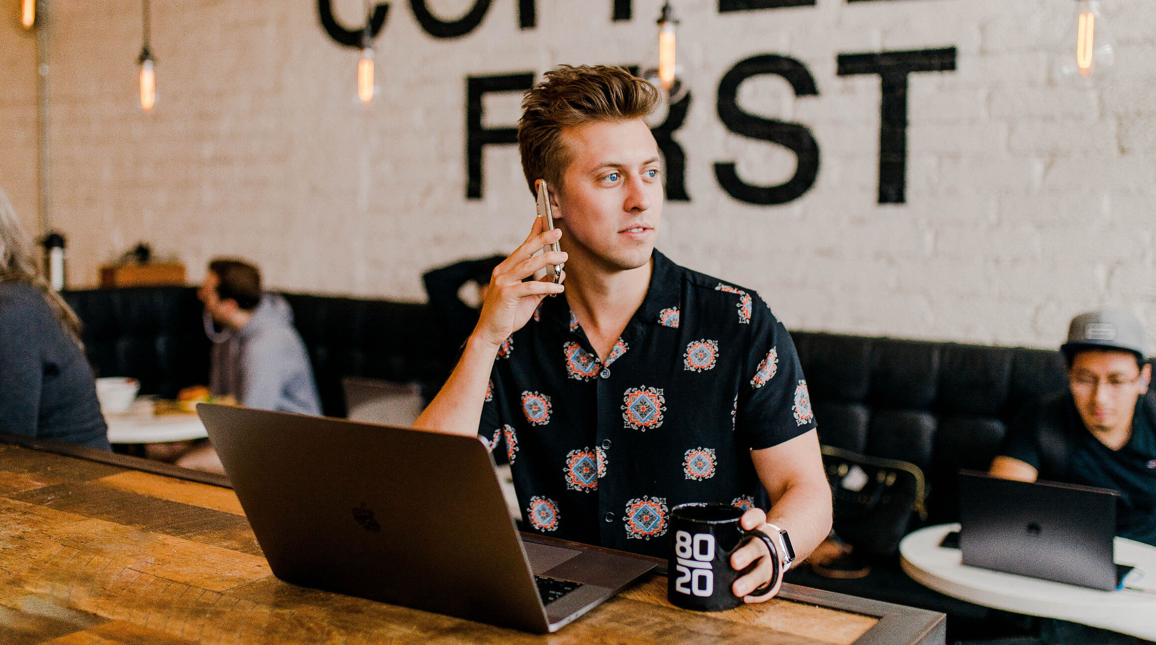 mężczyzna rozmawiający przez telefon i pracujący na laptopie w kawiarni