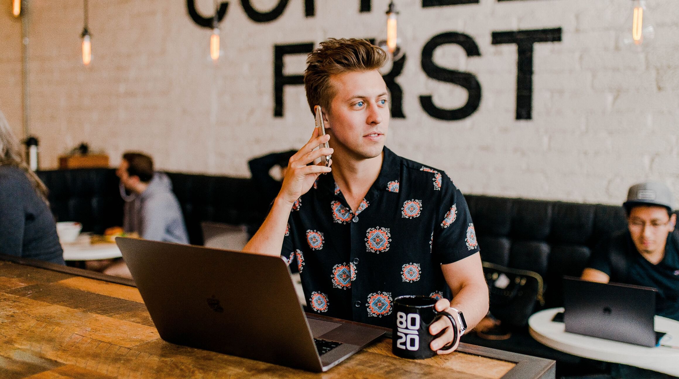 man talking on his phone and working on his laptop in a coffee shop