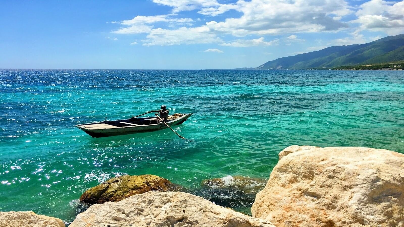 Three white-brownish rocks and a man riding a boat on the sea during daytime