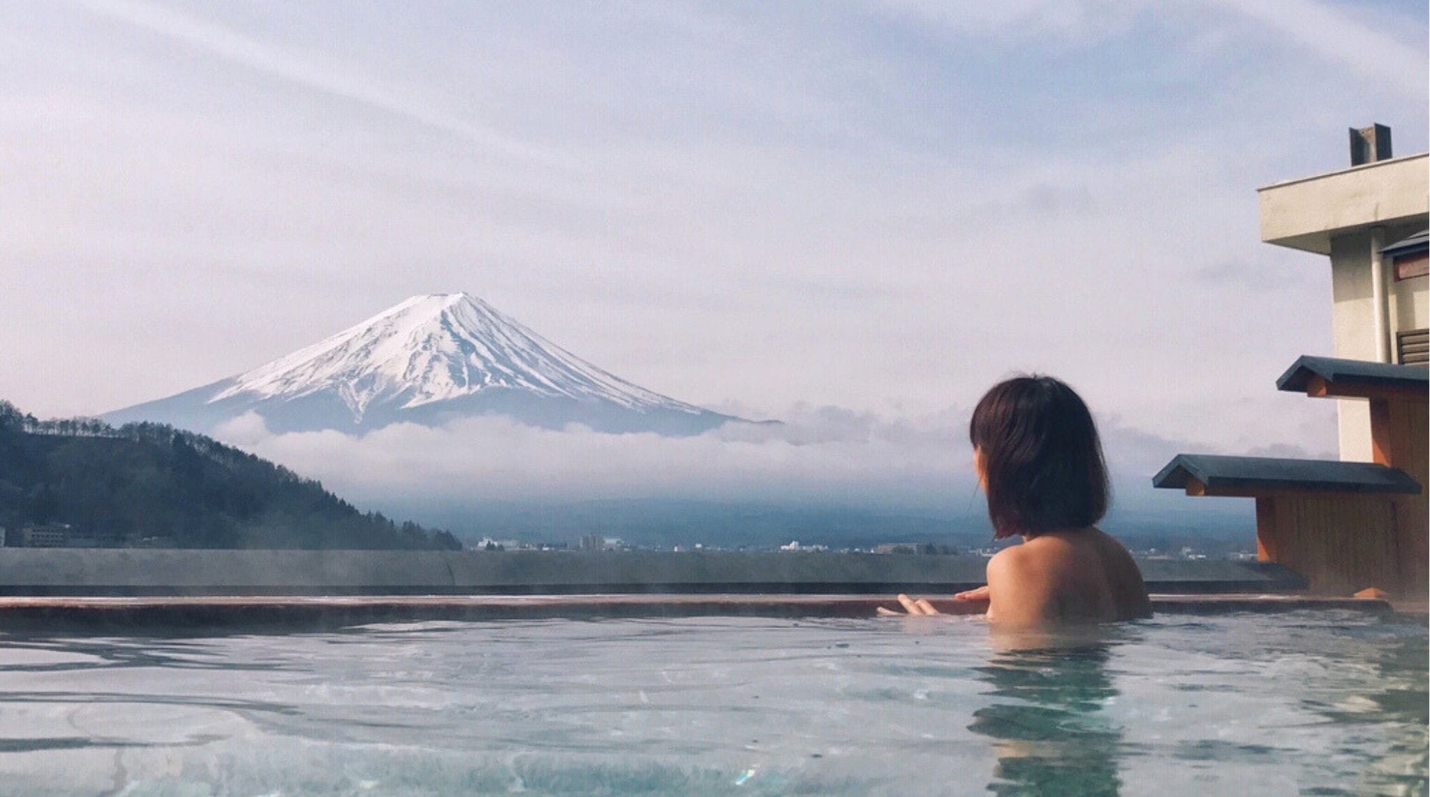 Mujer relajándose en aguas termales al aire libre con vista al Monte Fuji nevado.