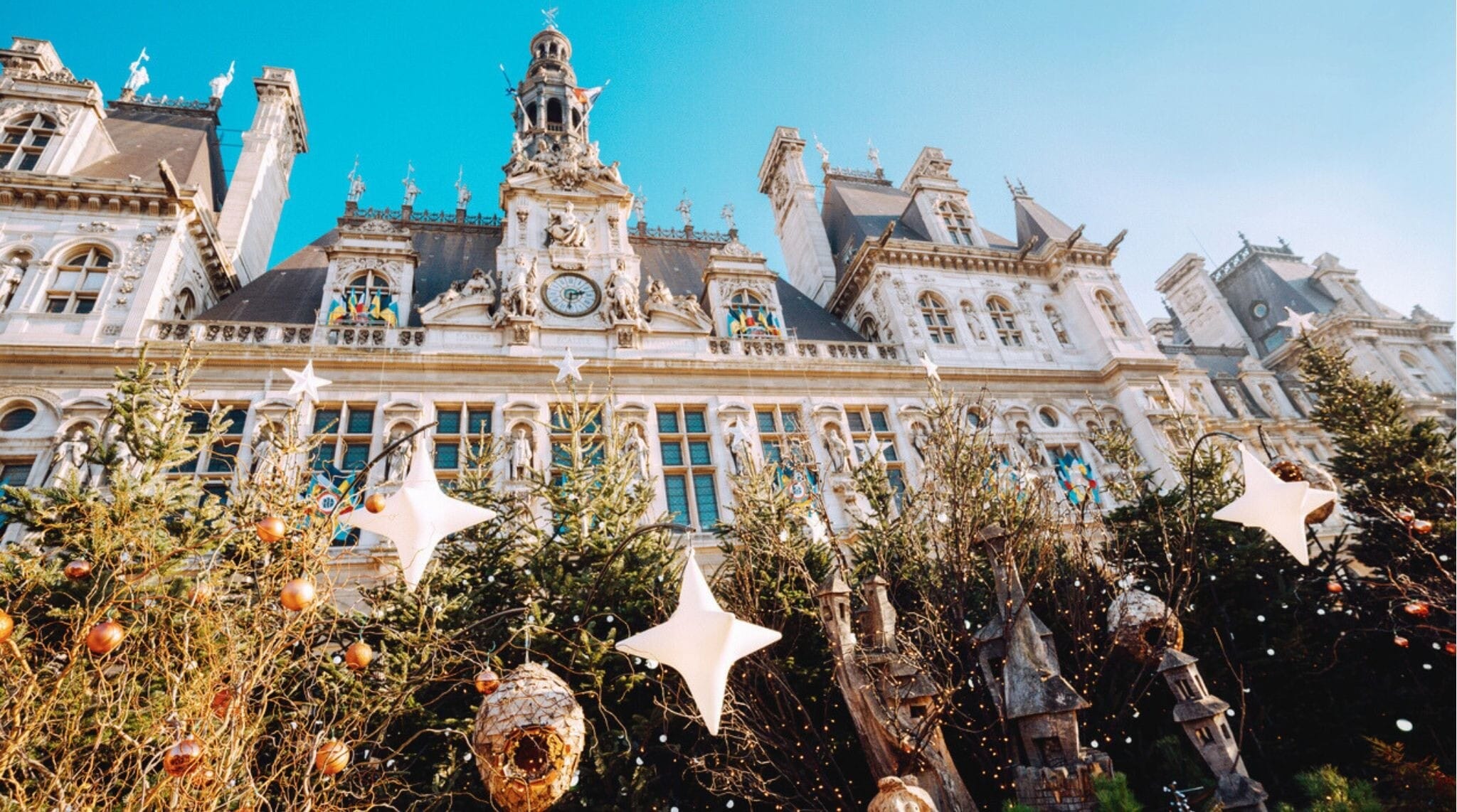 Fachada del Hôtel de Ville de París iluminada con decoraciones navideñas durante la temporada de invierno.