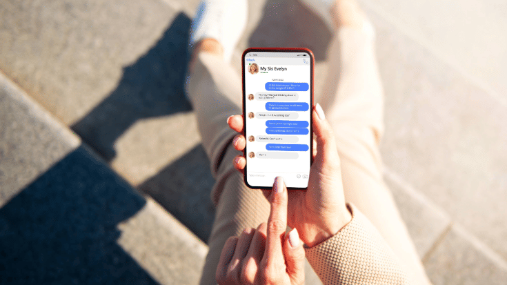 A person sitting outdoors holding a phone with a WhatsApp chat conversation open. The screen shows blue message bubbles, representing different WhatsApp text tricks such as WhatsApp bullet points, WhatsApp numbered lists, and how to change the font style in WhatsApp.
