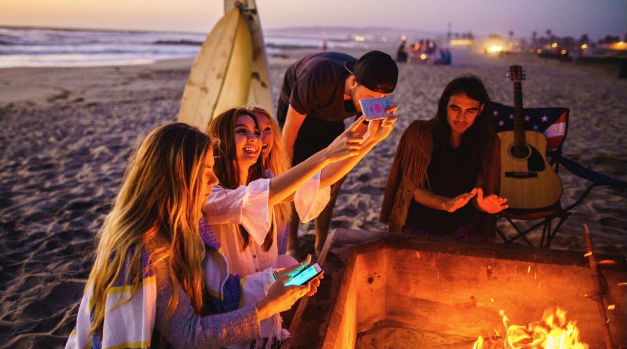 Grupo de amigos alrededor de una fogata en la playa de San Diego al atardecer.