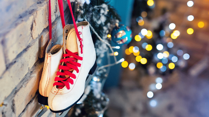 A photograph of some white ice skating boots tied by their red laces hanging up against a brown brick wall, to illustrate a blog post entitled 'Things to do in London in December'.