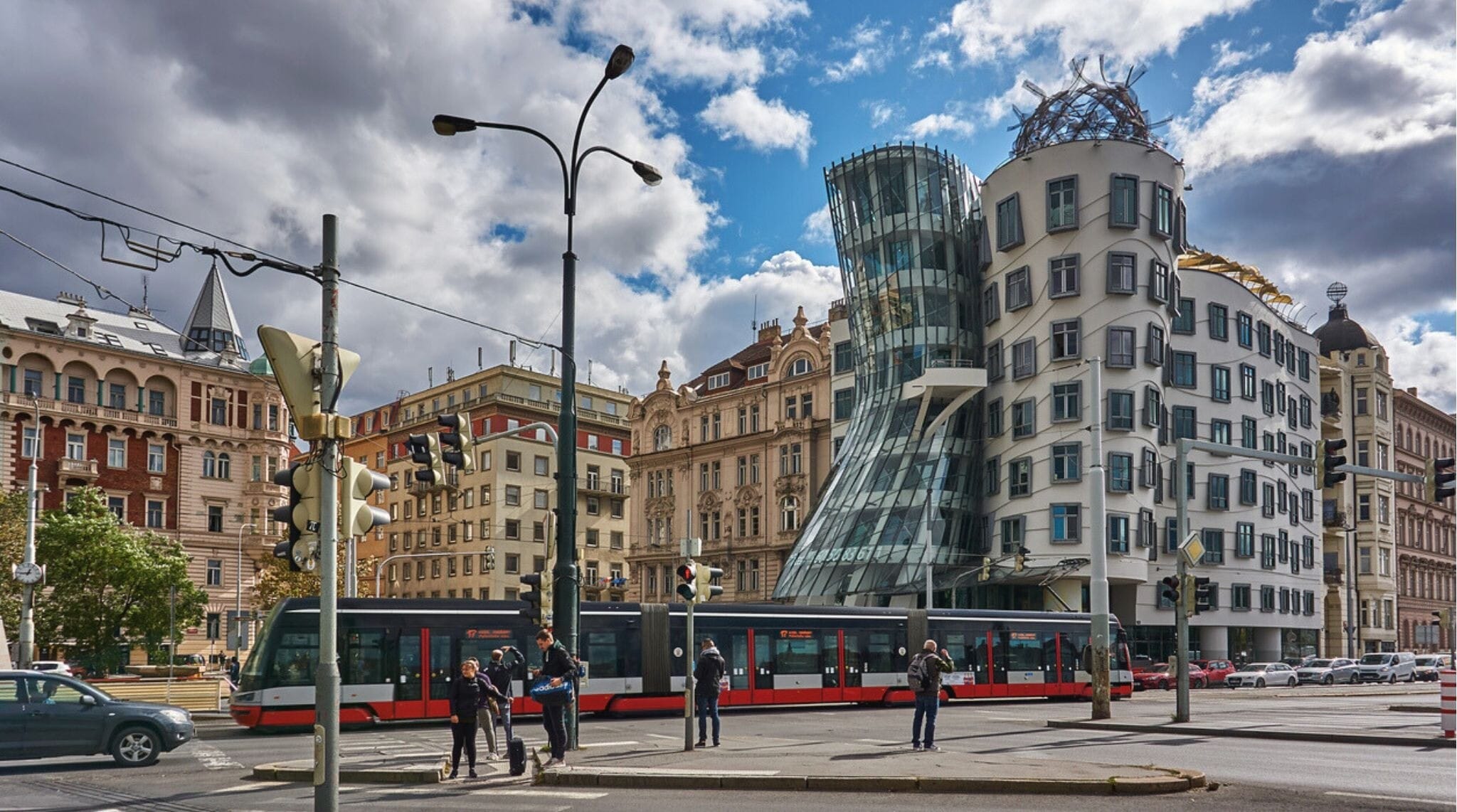 Pedestres, veículos e um bonde na rua Rašínovo Nábřeží. Ao fundo, o edifício Dancing House de Praga.