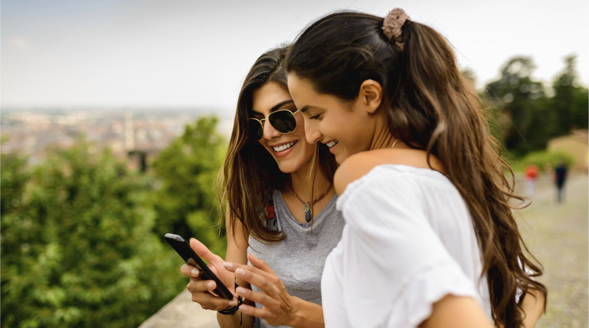 Dos jóvenes mujeres usando sus teléfonos móviles en un entorno urbano en Colombia.