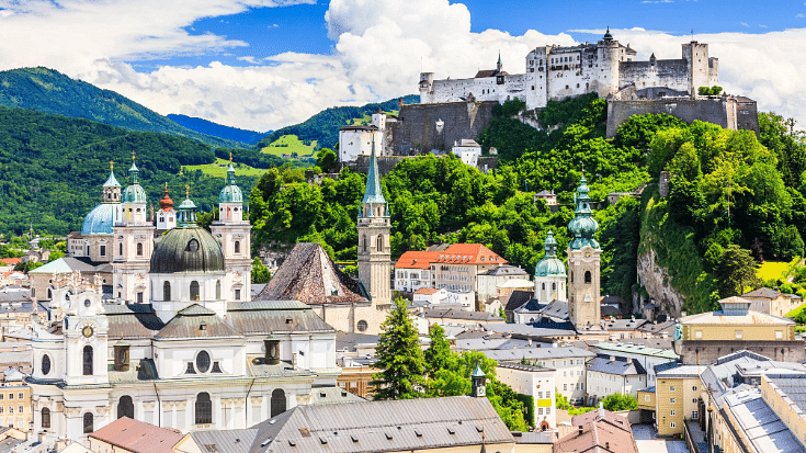 A picturesque view over the Austrian town of Salzburg with backgrounds of green hills and leaves, to illustrate a blog post entitled Trending Winter family holidays for Brits in 2024