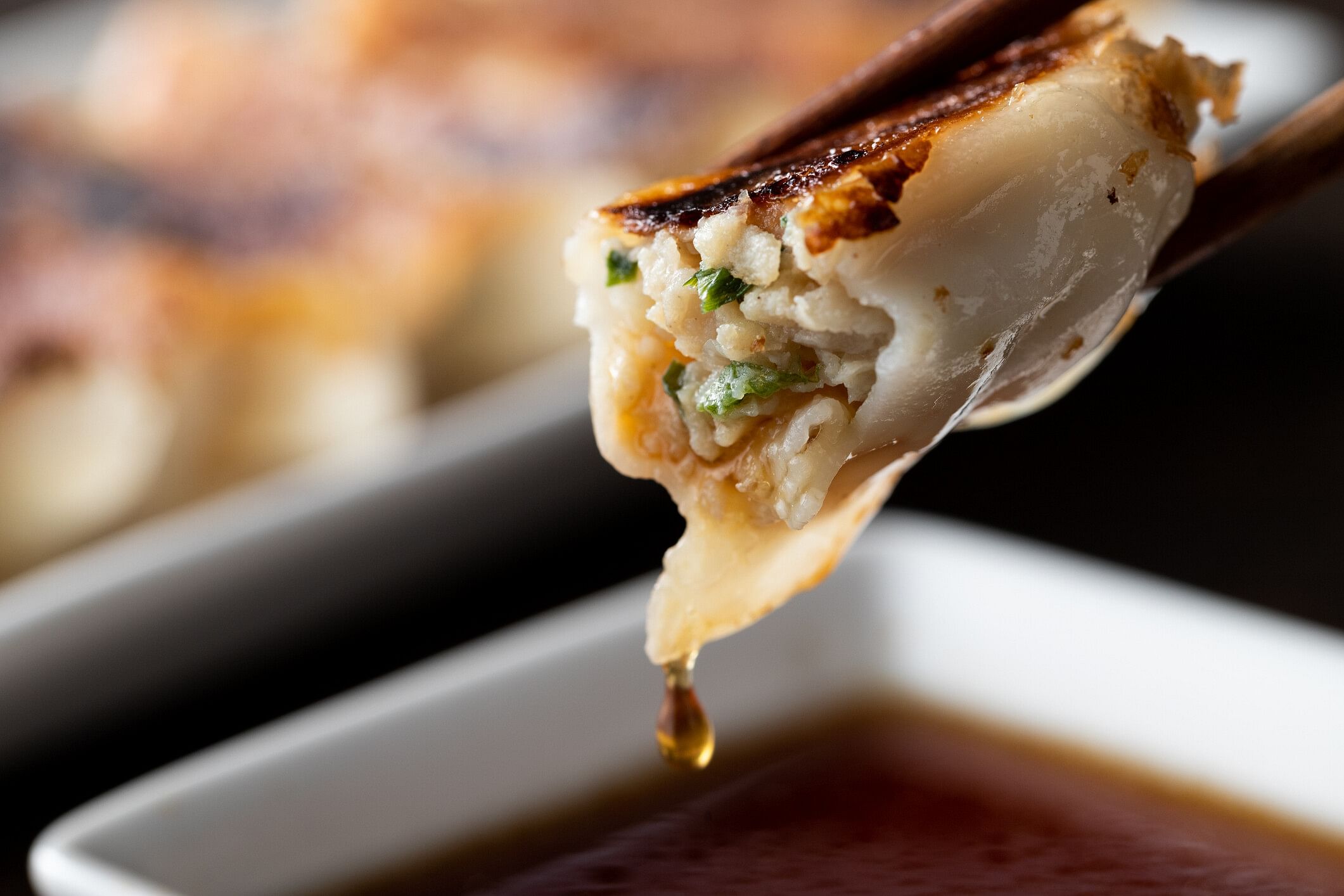 Gyoza held by a chopstick and dipped in soy sauce