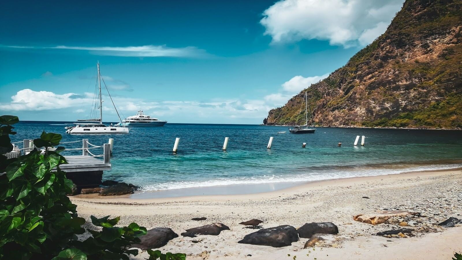 A beach with turquoise water, white boats and a huge mountain during the day