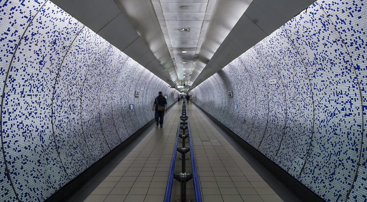 An image of a person from behind, slightly blurry, as they run through a London Underground tunnel to catch a train on the Piccadilly Line, to illustrate a blog post entitled 'The Cheapest way to go to Heathrow Airport from London'.