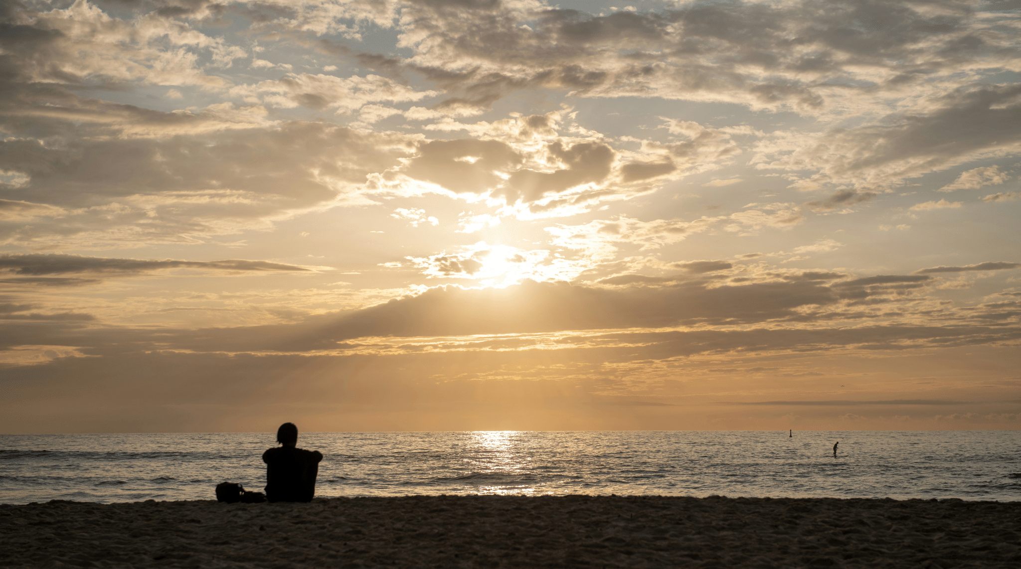 Person sitzt während des Sonnenuntergangs am Strand