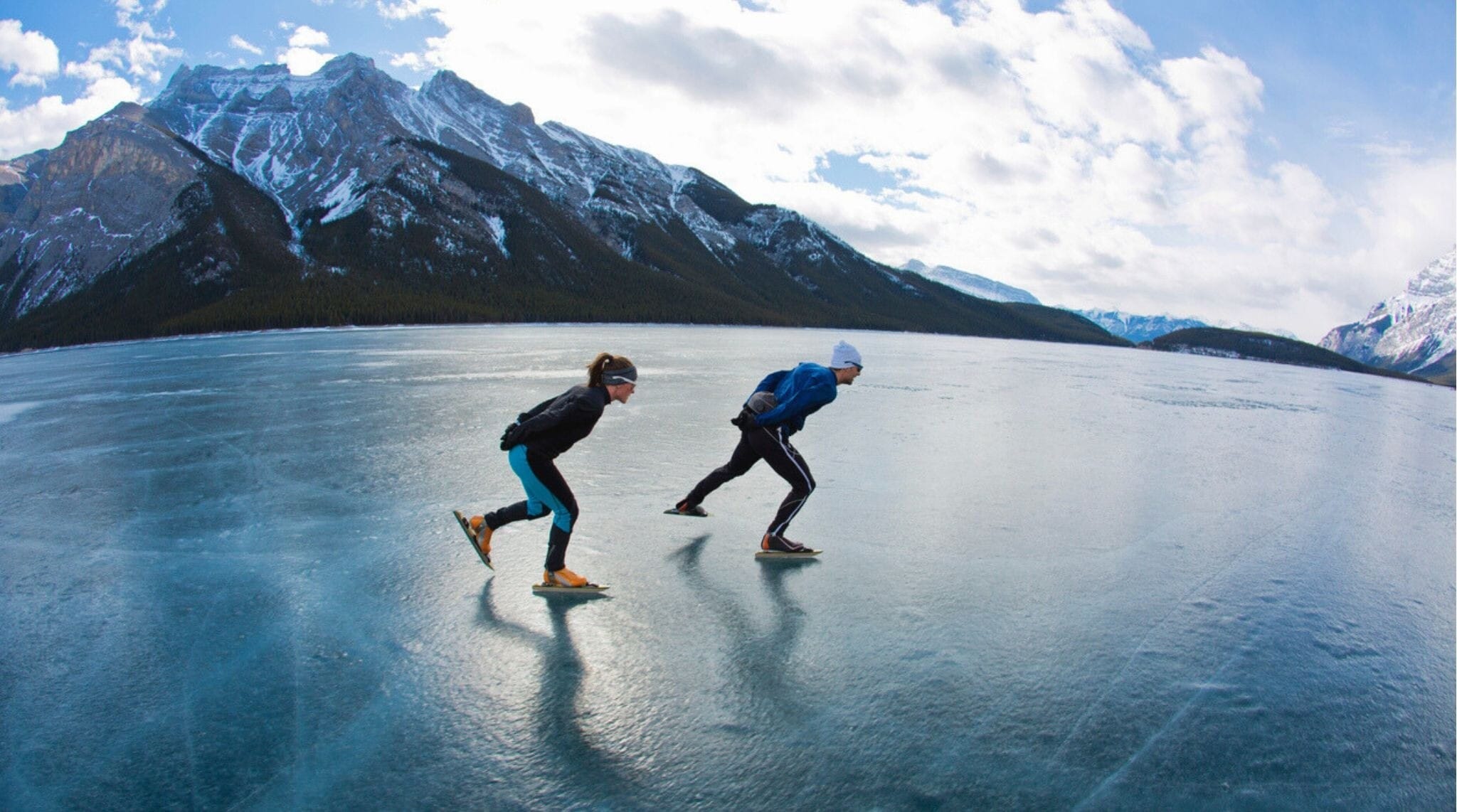 Um homem guia uma mulher em uma aventura de patinação de velocidade no gelo no Lago Minnewanka, no Parque Nacional Banff, Alberta, Canadá.