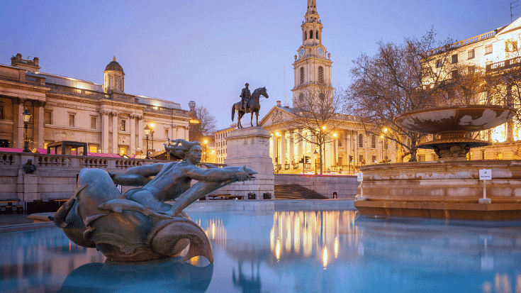 A photograph of Trafalgar Square in London, with a nautical statue in the foreground and a fountain, to illustrate a blog post entitled 'How to Spend New Year's Eve in London'.