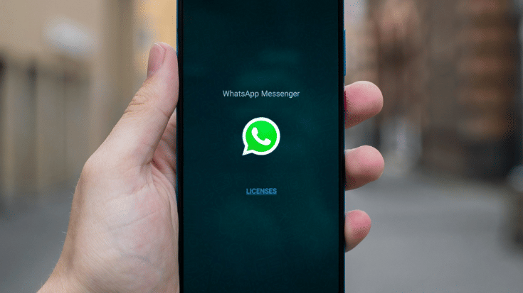 Close-up of a hand holding a phone showing the WhatsApp Messenger start screen with the green logo on a dark background. Ideal for illustrating advanced WhatsApp text tricks including bold, italics, strikethrough, and Monospace WhatsApp text formatting.