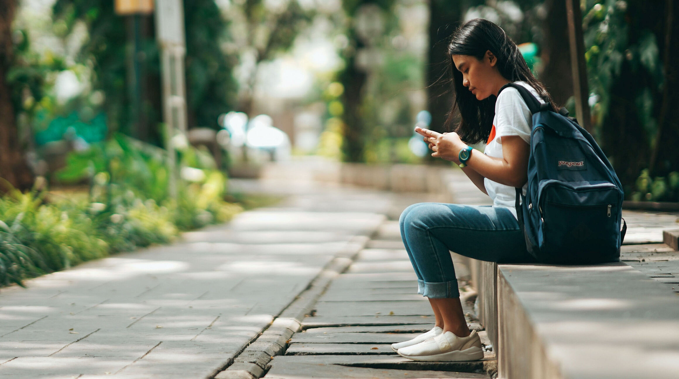 Mädchen sitzt auf dem Bürgersteig und benutzt ihr Smartphone