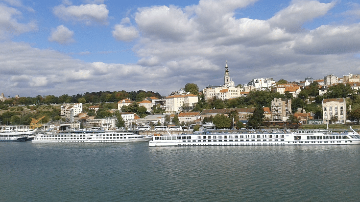 An image of boats on the Danube River as it runs through Belgrade, with buildings as a blue sky overhead, to reference the city in a blog post entitled Extreme Day Trips Abroad from the UK.