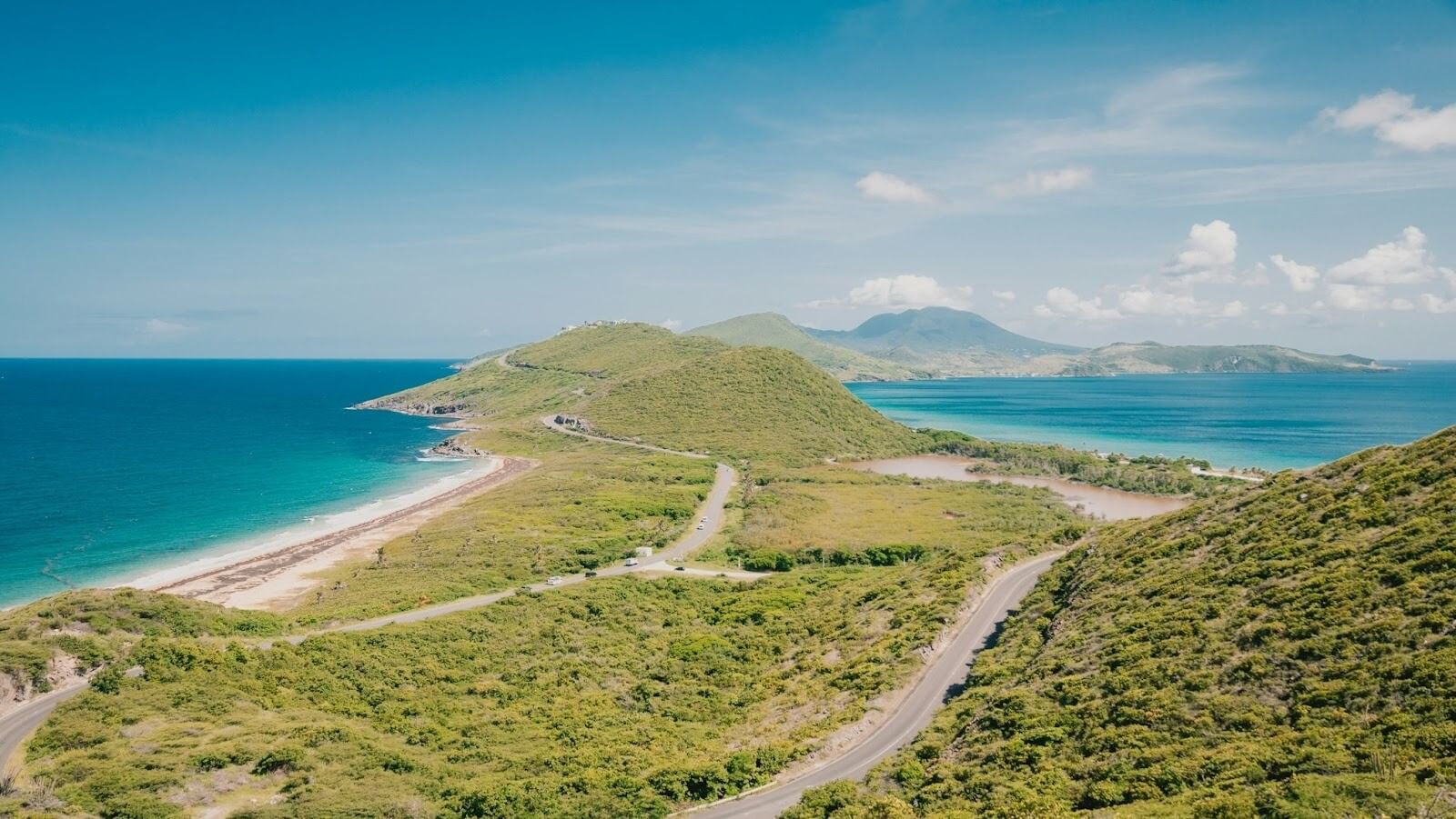 Coastal view with winding roads, vegetation, surrounded by a large body of water and distant mountains
