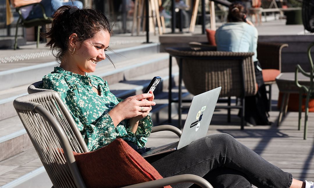 Açık havada bir masada oturan ve akıllı telefonuna bakan kız 