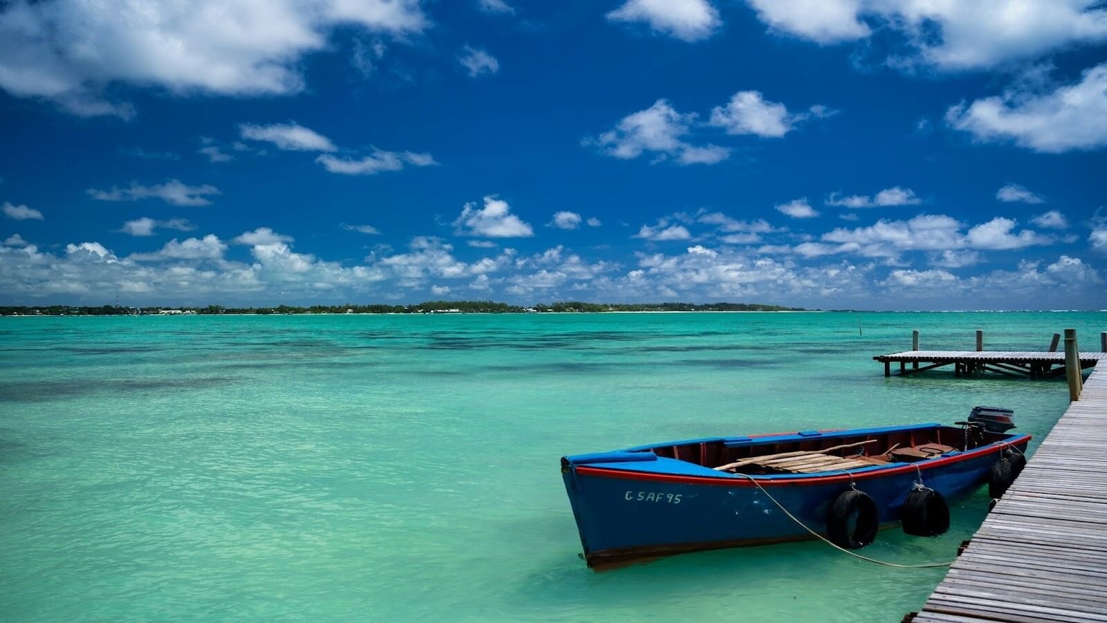 Red and blue boat achored to a deck on large body of water