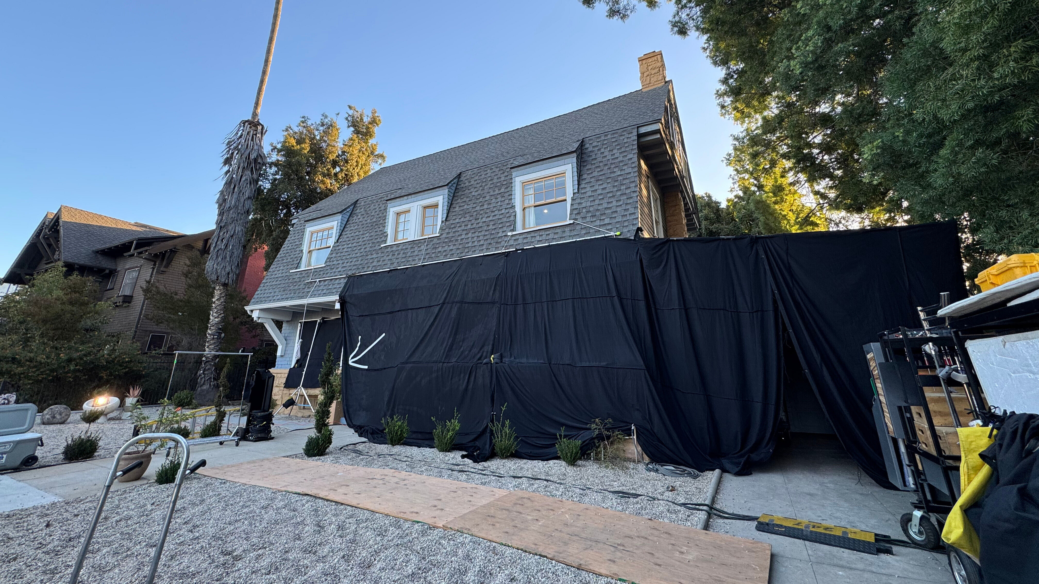 A residential home in Los Angeles, draped in black tarps, surrounded by film equipment