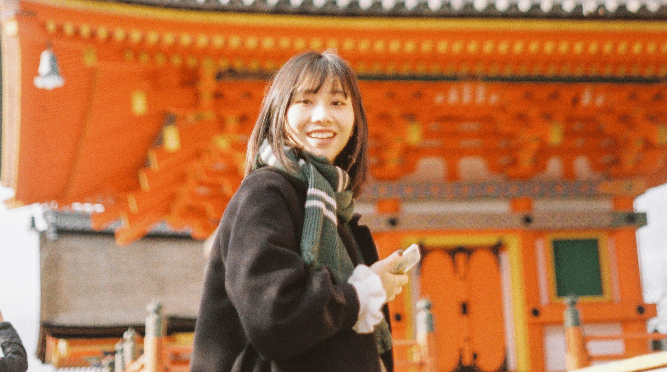 Turista sorridente usando o celular em frente a um templo tradicional no Japão, conectada com chip internacional Japão.