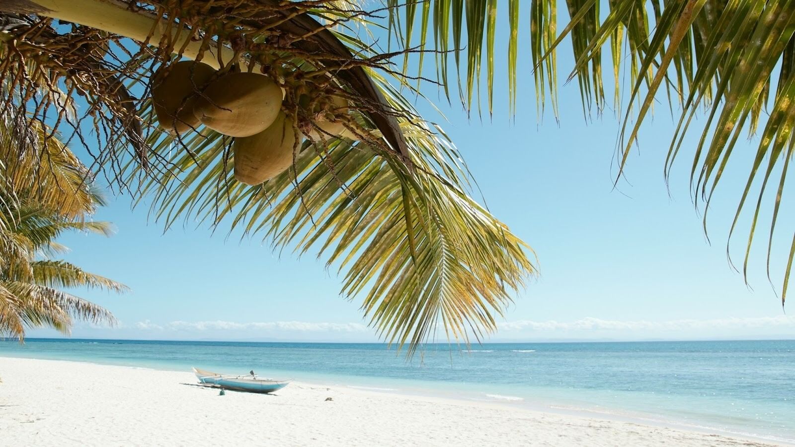 Beach with white sand, one boat ashore and coconut trees