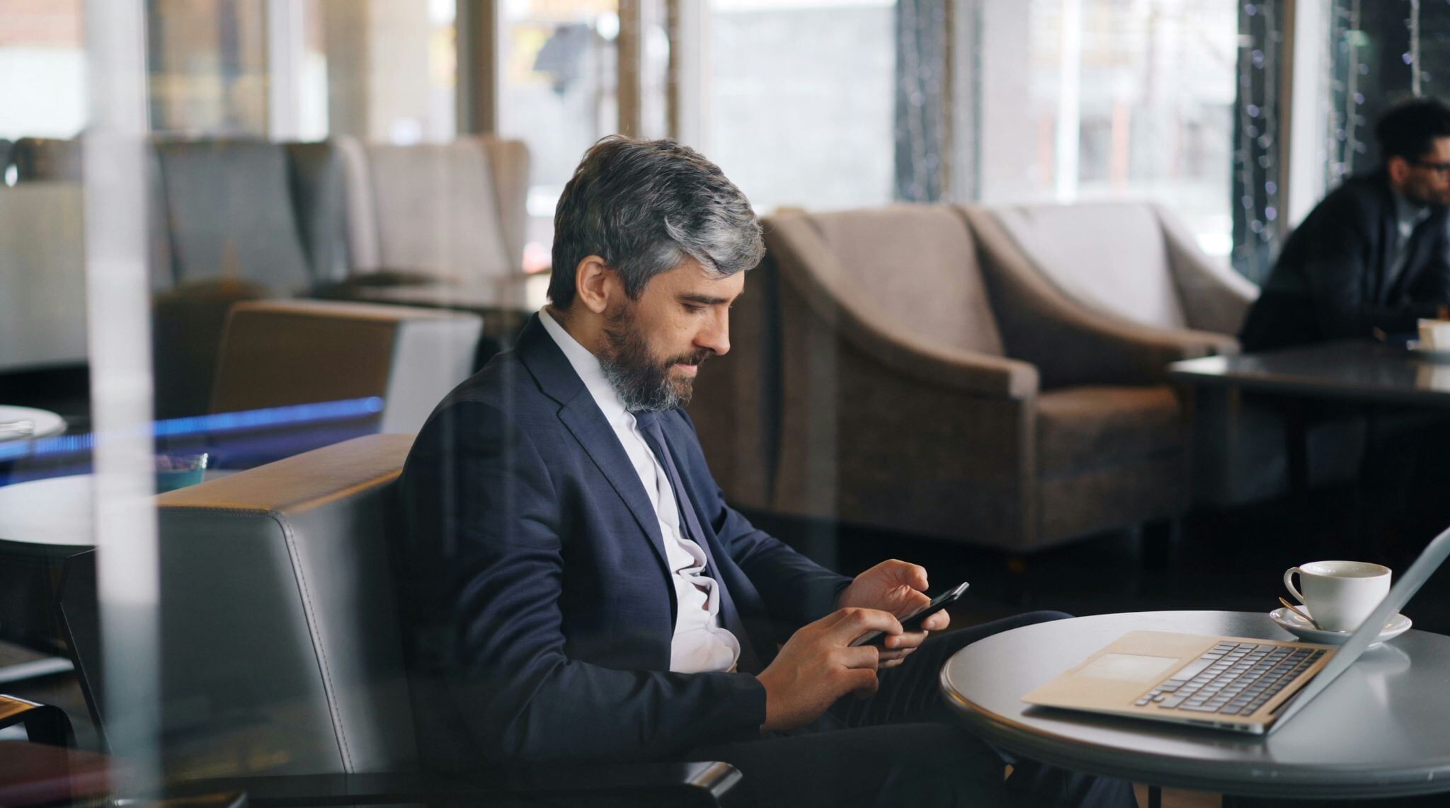 ラウンジでパソコンとスマホを使って仕事をするビジネスマン