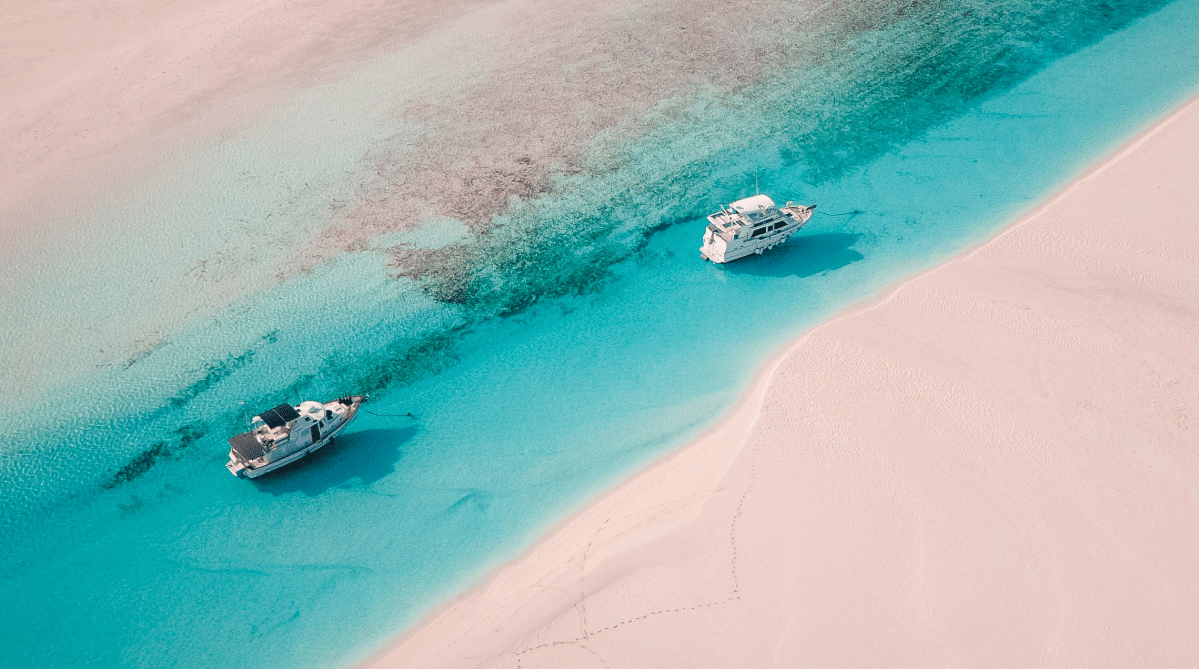 Two boats moored next to pink sand in the Bahamas
