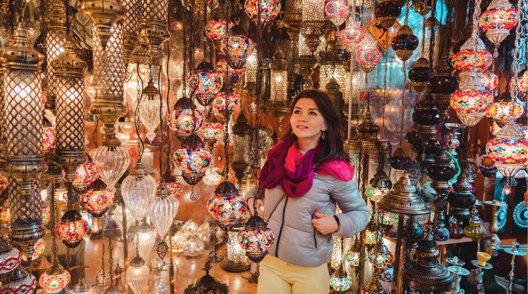 Mulher sorridente admirando lâmpadas turcas à venda no Grande Bazar, em Istambul, Turquia.