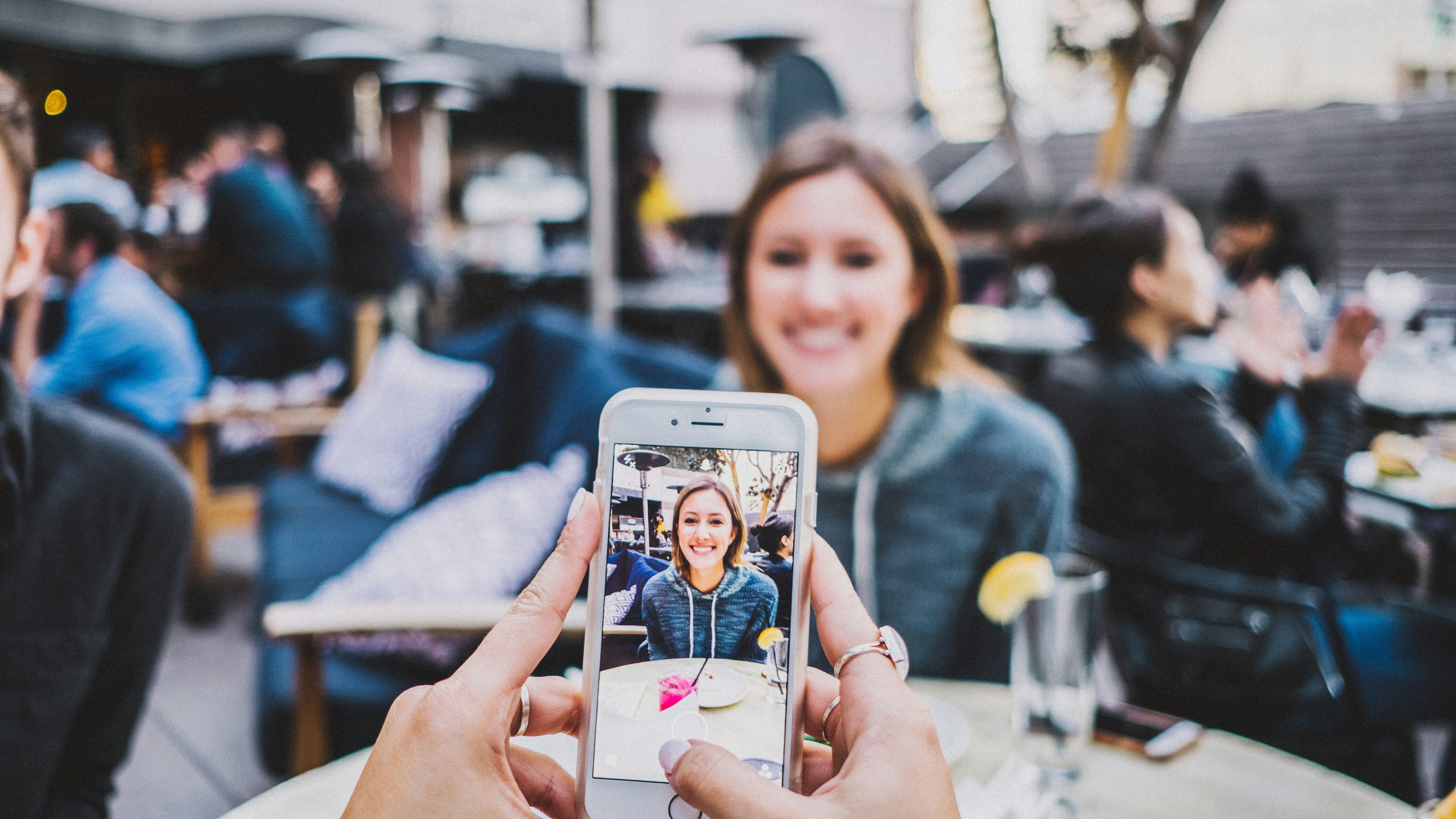 Two people in a crowded restaurant patio taking photos and videos of each other