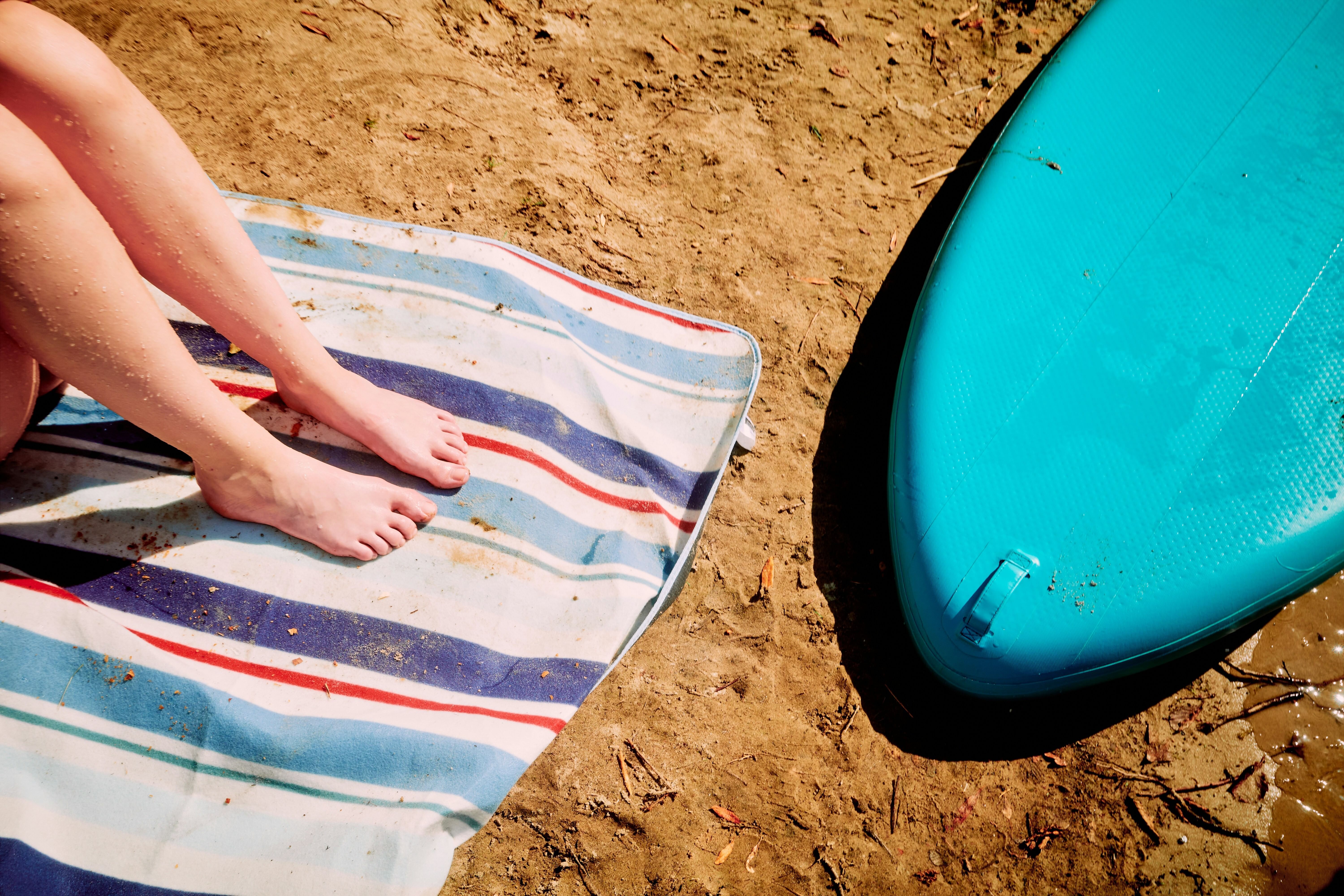 Woman's feet on a towel next to a surfboard