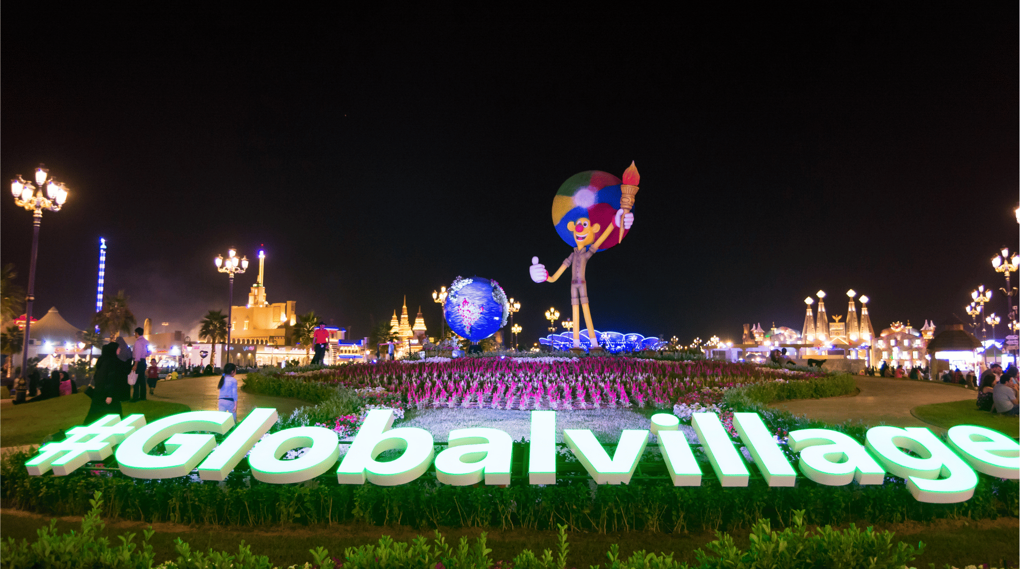 مدخل القرية العالمية دبي ليلًا مع شعار جلوبال فيليدج بالإنجليزية وإضاءة مبهرة وازدحام الزوار في موسم 2025