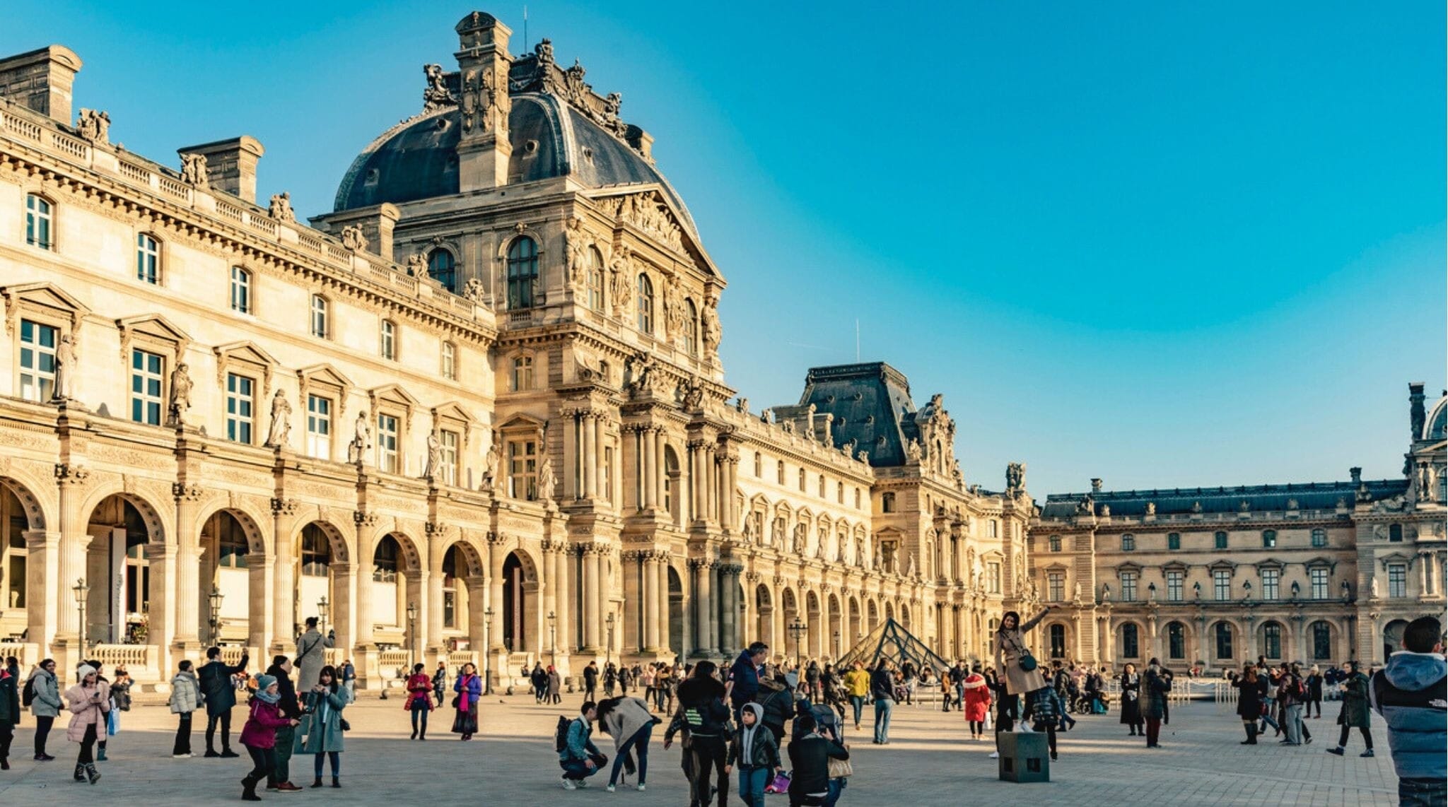 Turistas reunidos frente a la pirámide del Museo del Louvre en un día frío de invierno en París.