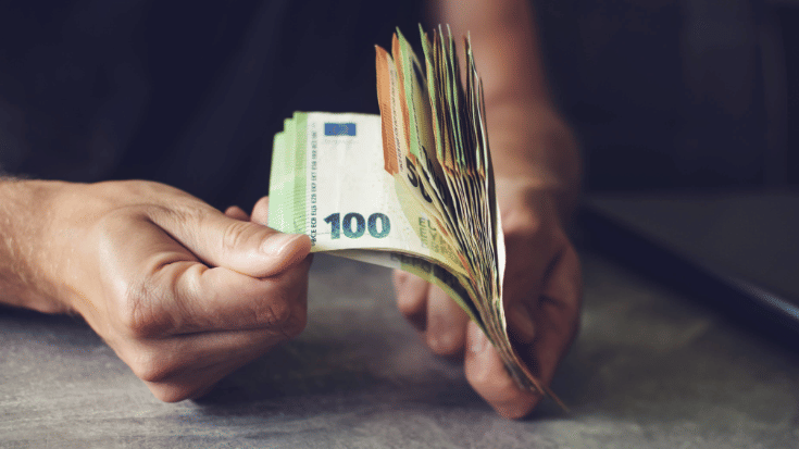 A photo of a close up of a man's hand, as it leafs through a wad of Euro notes. To illustrate a blog post entitled 'Where is Hot in November in Europe?'