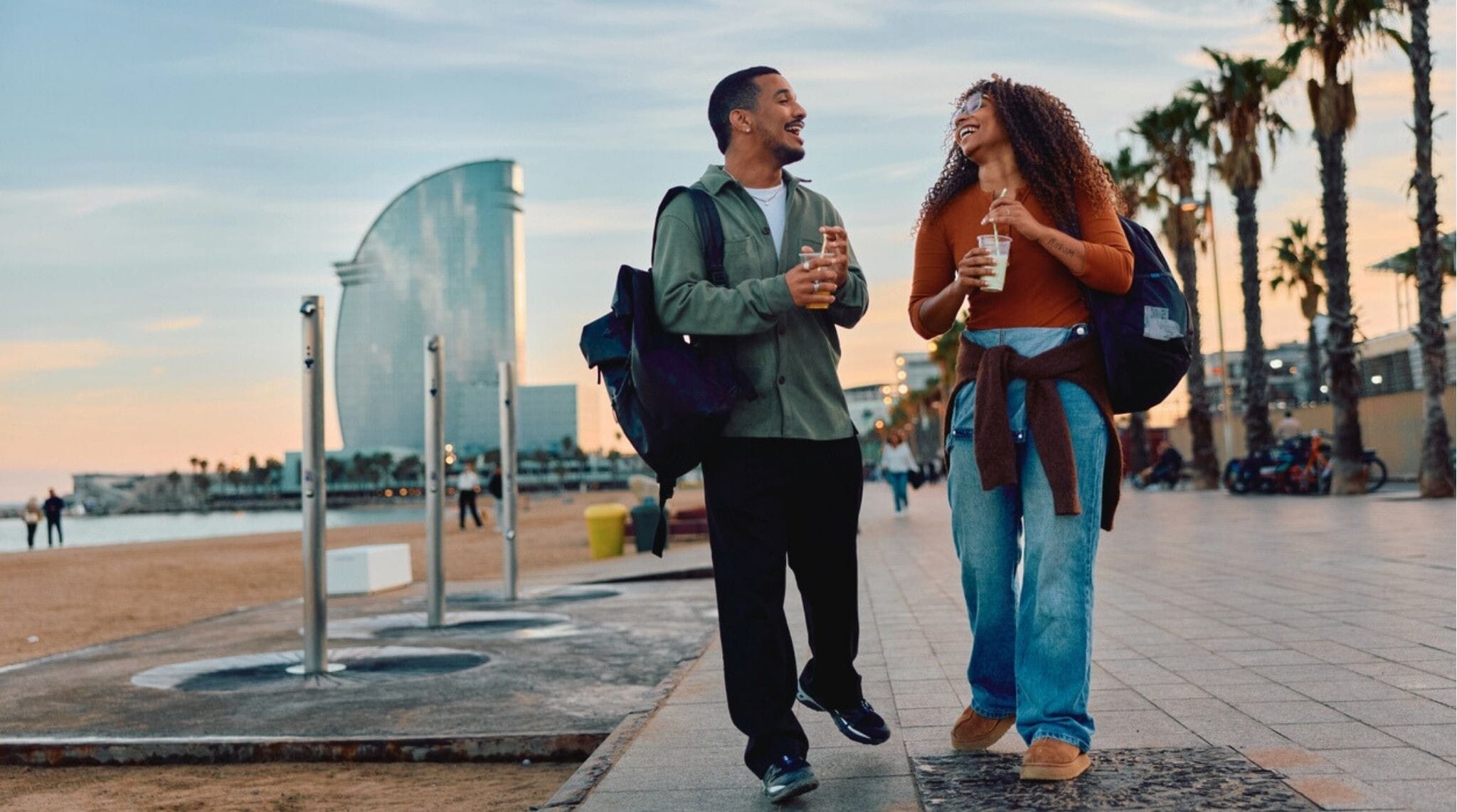 Pareja caminando por la playa de Barcelona al atardecer con copas en la mano