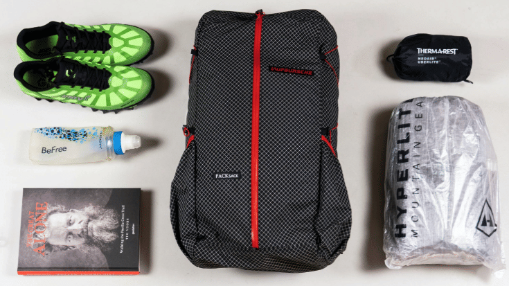 A colour photograph of a plain white floor with someone's holiday packing spread out on it. There are a pair of neon green trainers, an empty water bottle, a backpack and some clothes wrapped tightly in waterproof plastic. There is also a paper book. To illustrate a blog post entitled 'Berlin Half Marathon 2026: Can You Still Register?'