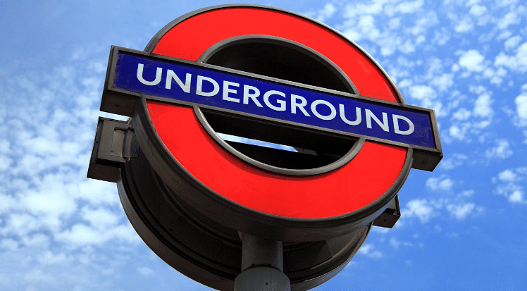 A generic sign for a London Underground station, which is a red circle with a blue line crossing it in the middle, with the words 'underground', to illustrate a blog post entitled The Cheapest Way to Get to Heathrow Airport from London.