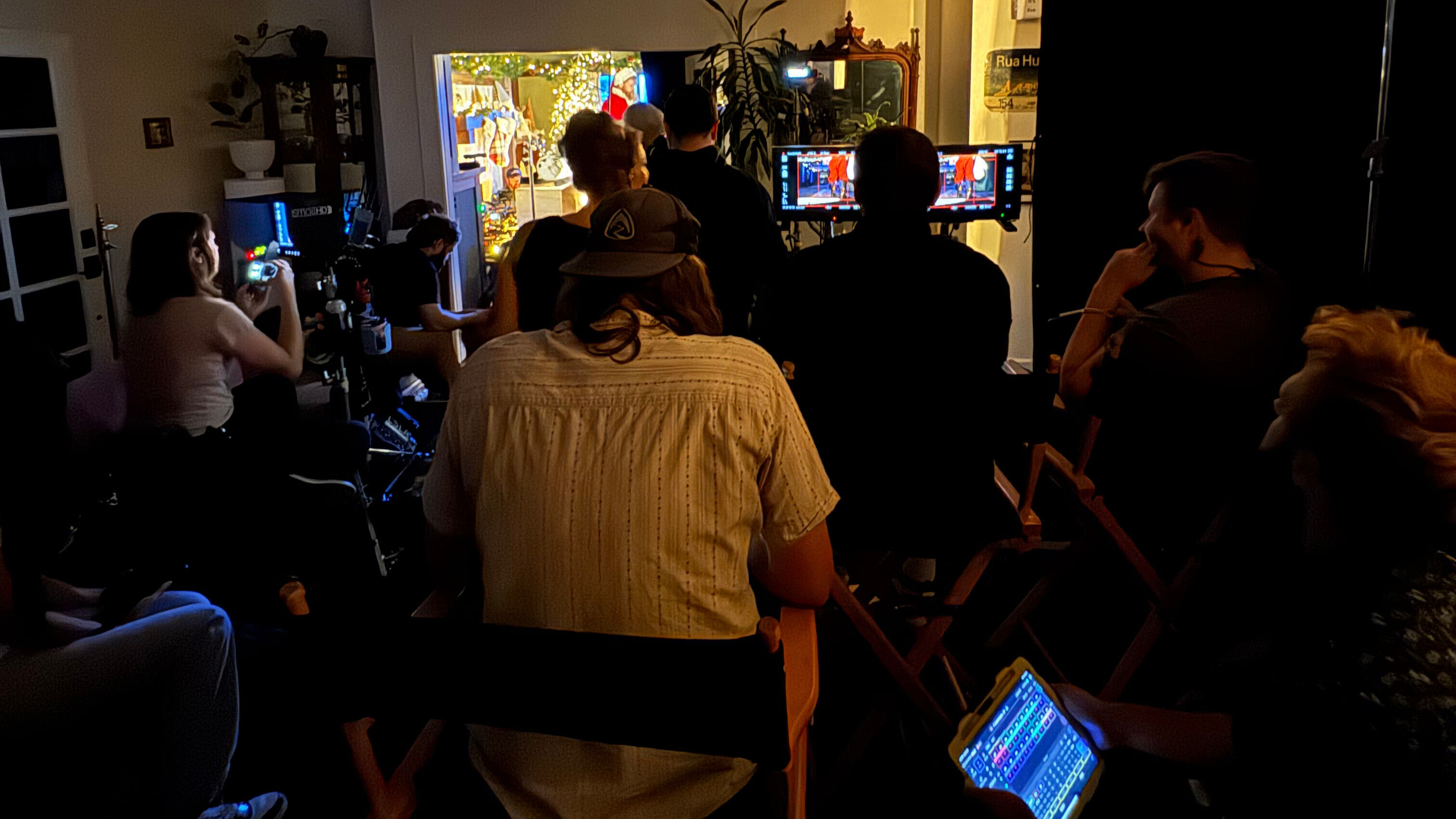 A quiet film set of the crew behind the scenes, sitting quietly in the dark while a scene takes place in an adjacent room