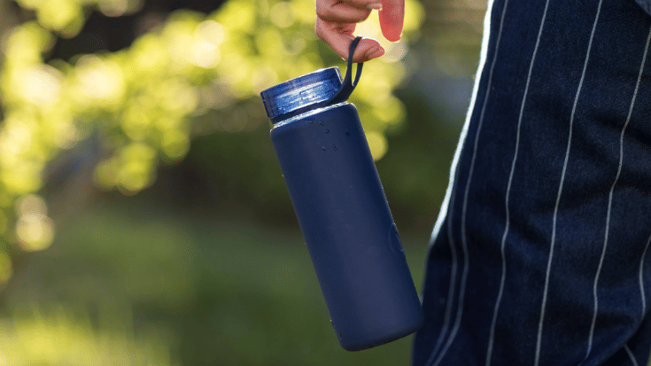 A photograph of a close-up image of a hand holding a refillable blue plastic water bottle. To illustrate a blog post entitled 'The Ultimate Sziget Festival Guide.'
